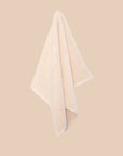 Chunky cotton weave bathmat in ecru colour hanging on a soft beige background. 