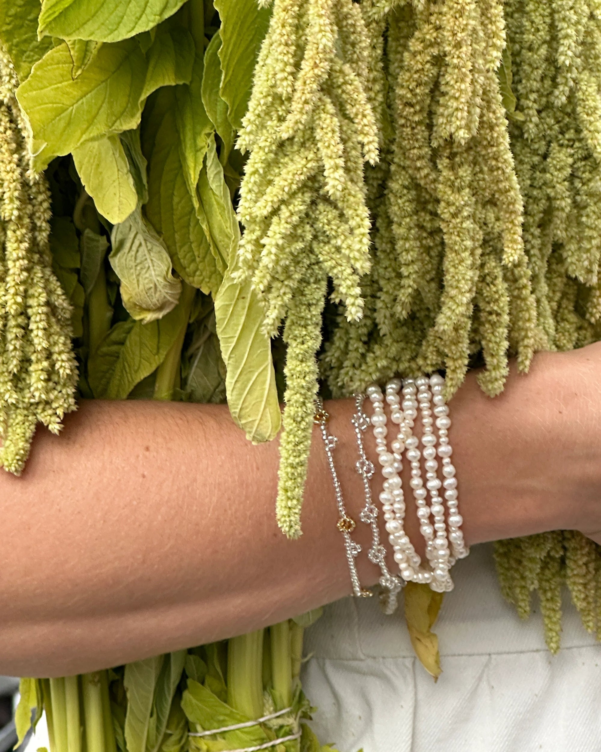 Close-up of a person's arm with green leaves and plants, wearing pearl bracelets.
