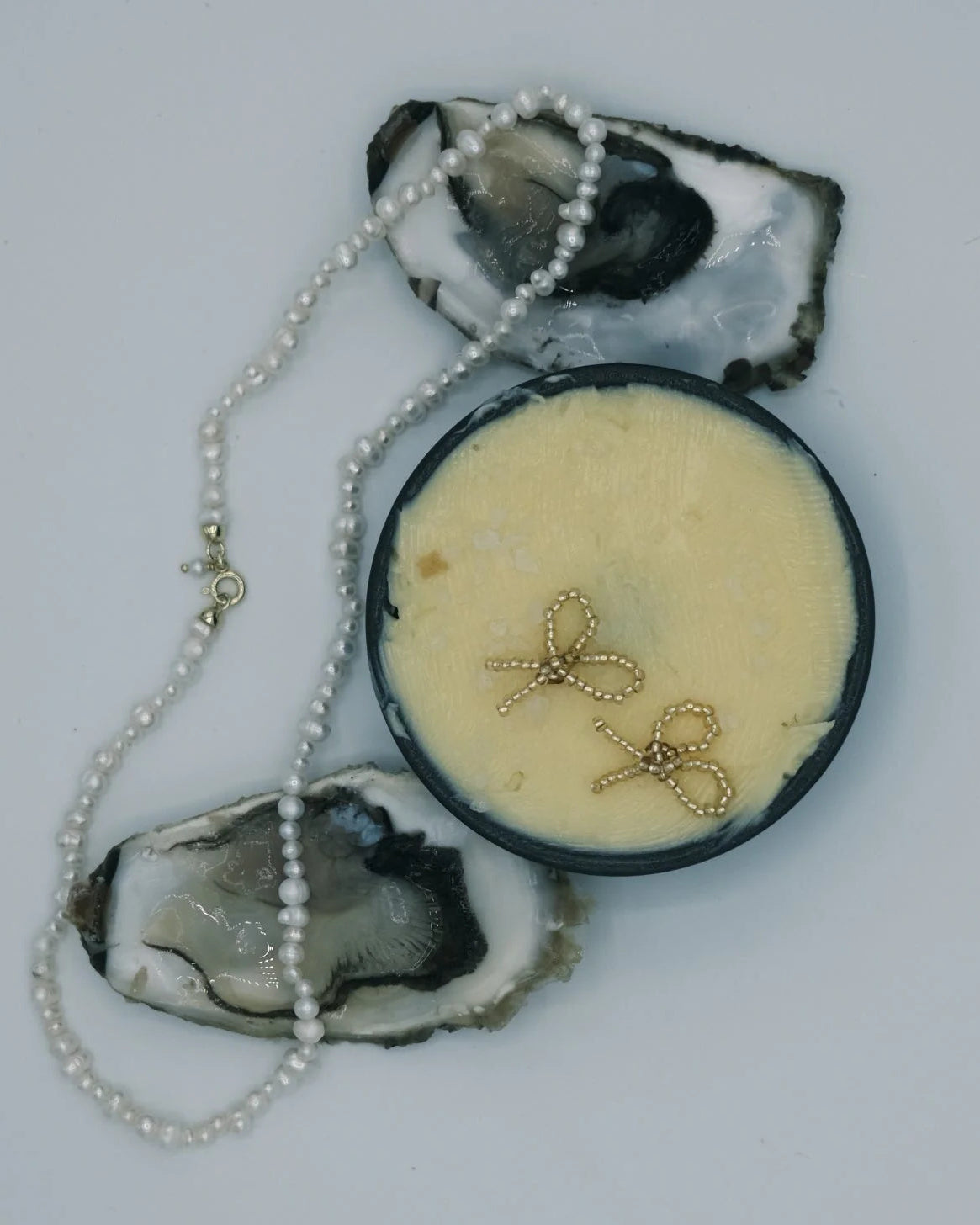 Gold beaded bow earrings and a pearl necklace displayed on oyster shells with a white background.