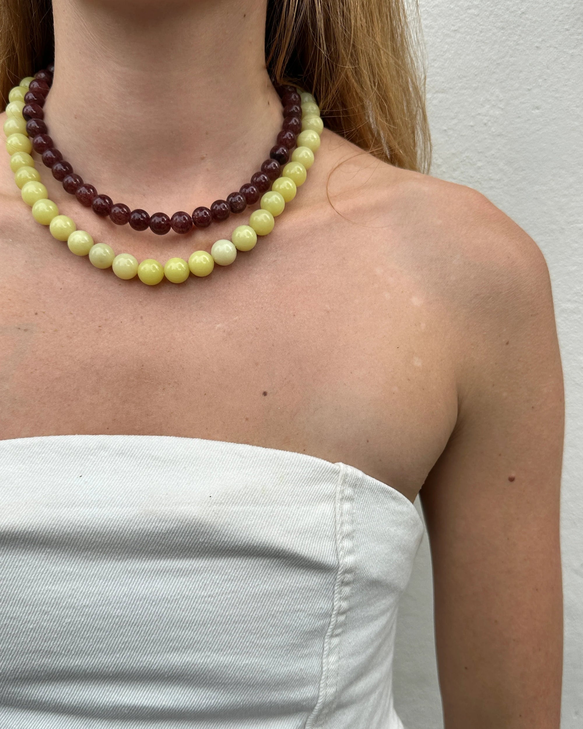 Person wearing a multicolored beaded necklace and white garment against a plain background