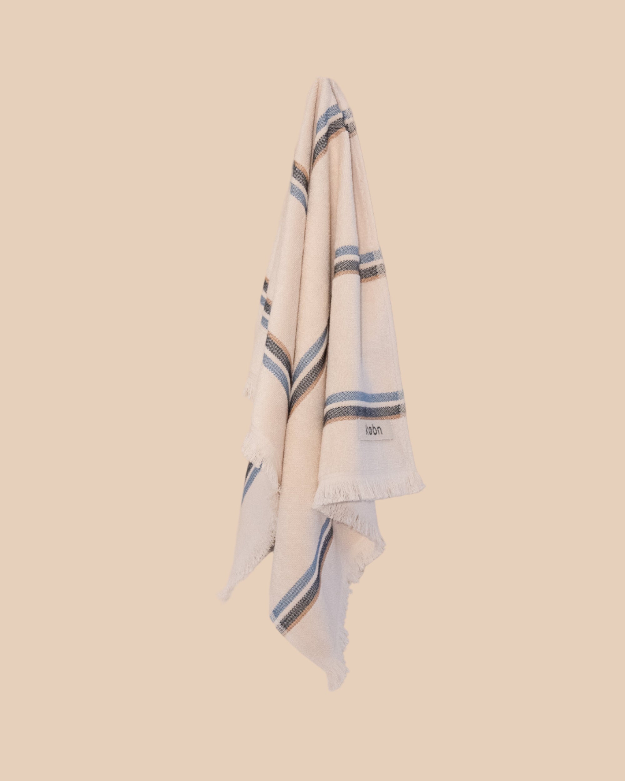 Ecru hand towel with blue stripes hanging on hook with butter yellow background
