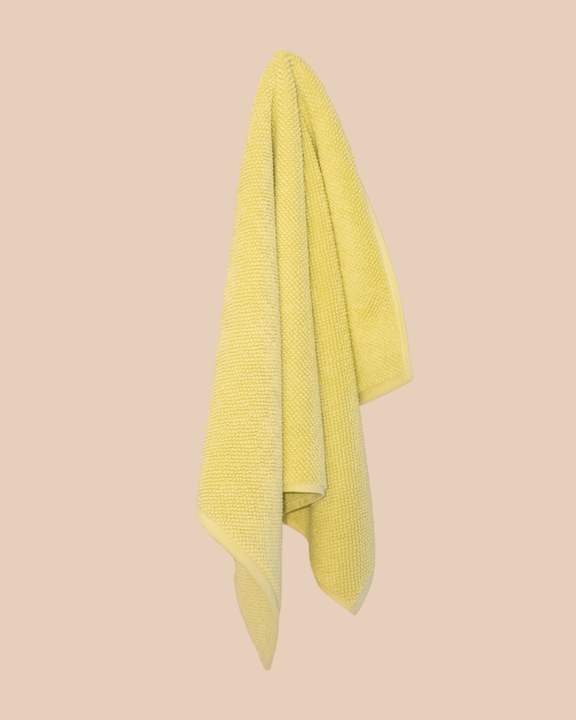 Textured yellow bathmatl hanging against a beige background