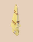 Bright yellow hand towel with brown stripes hanging on a netural wall.