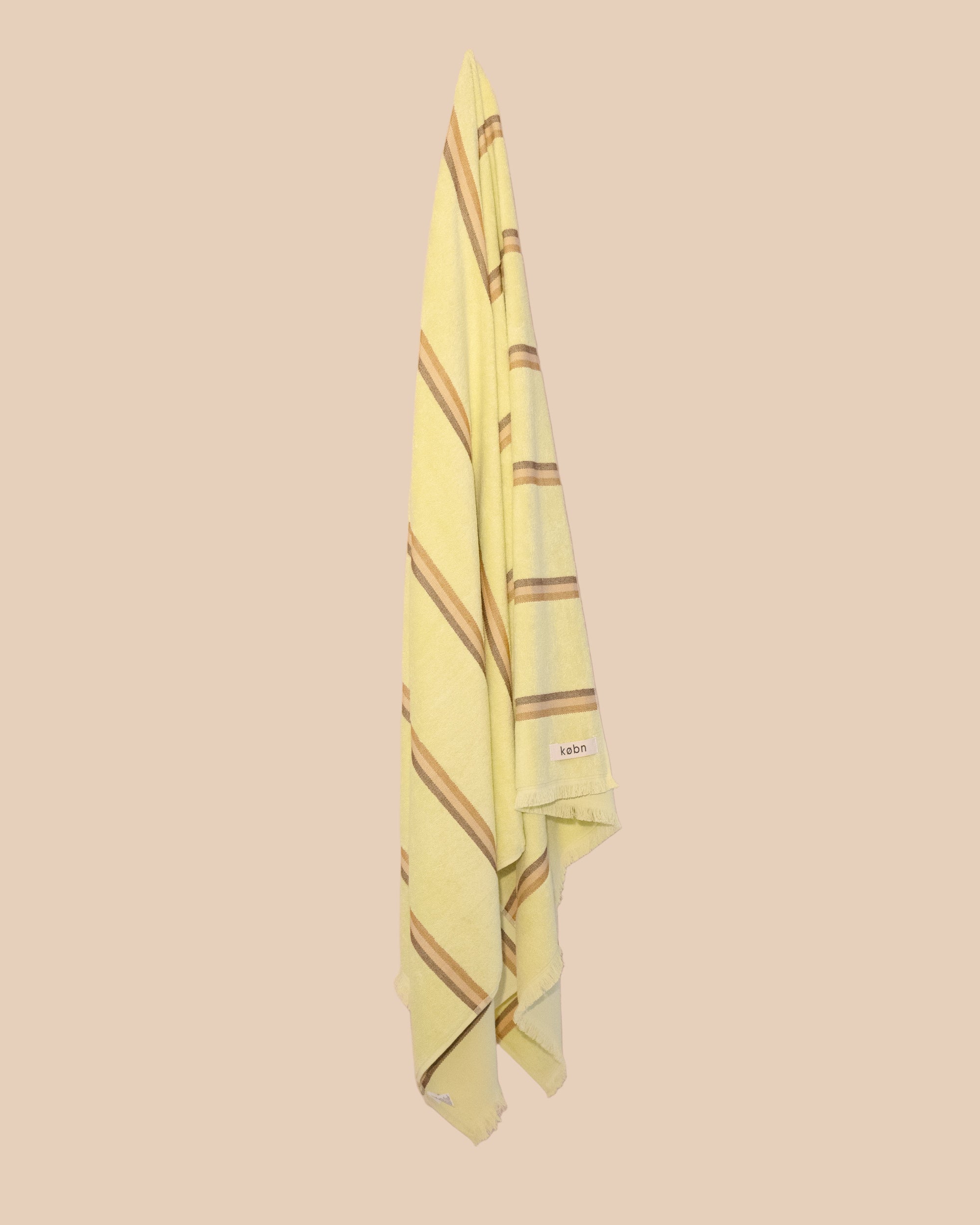 Bright Citrus Turkish towel with stripes and fringing by kobn hanging on a butter yellow background