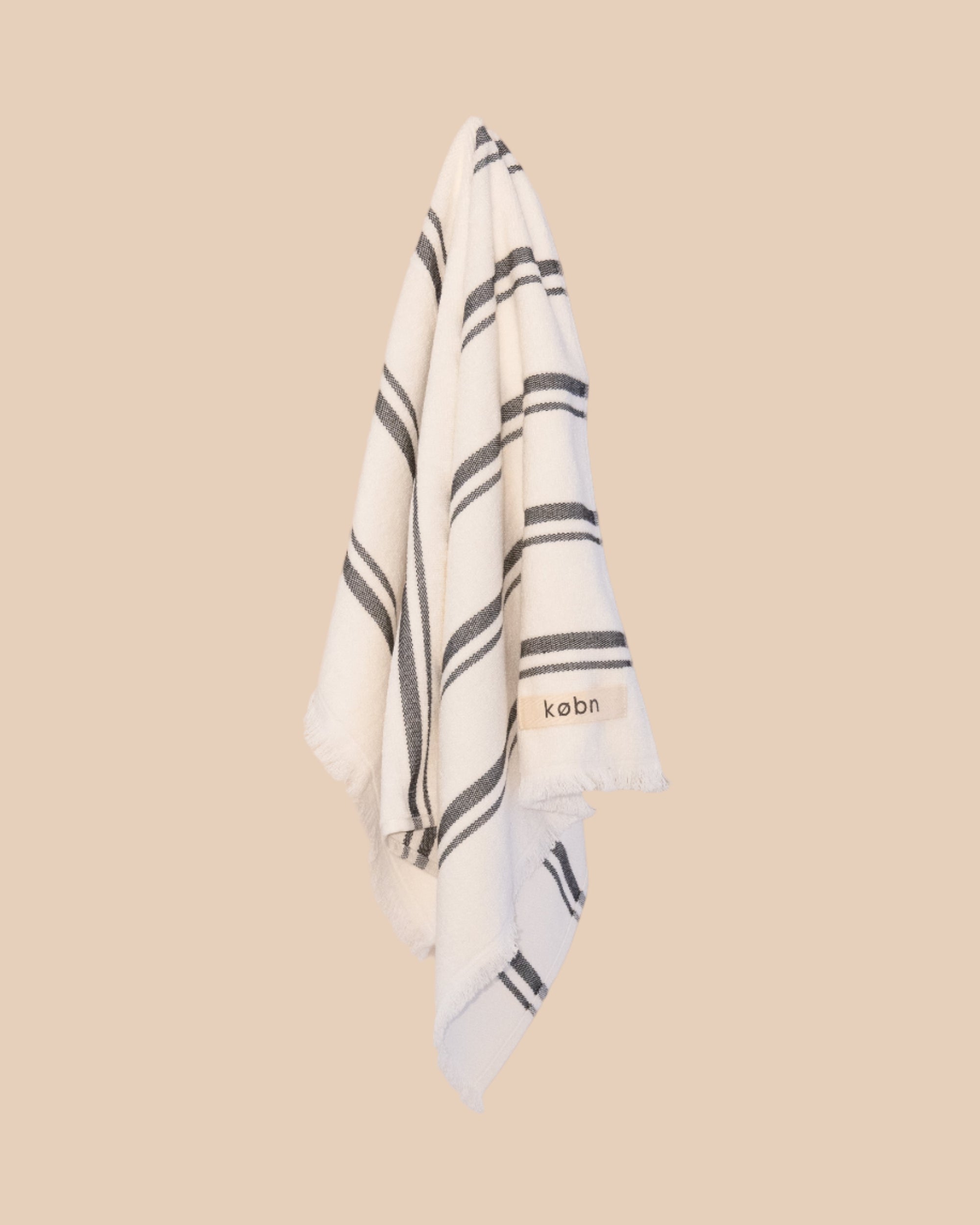 White hand towel with black stripes and 'kobn' branding on a beige background