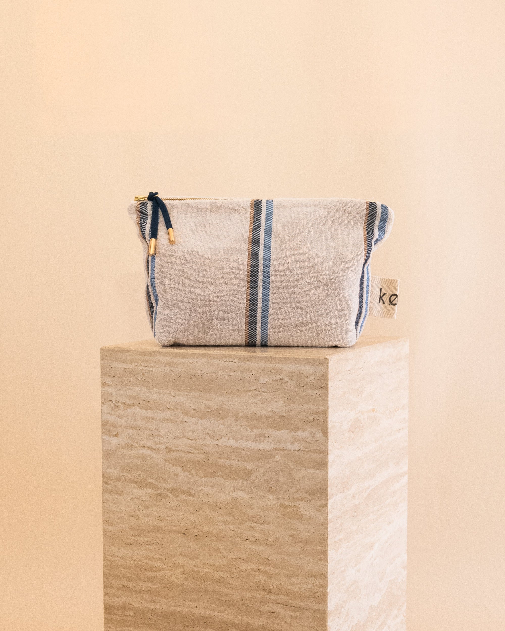 Terry towelling soft pouch with blue stripes sitting on a travertine plinth

