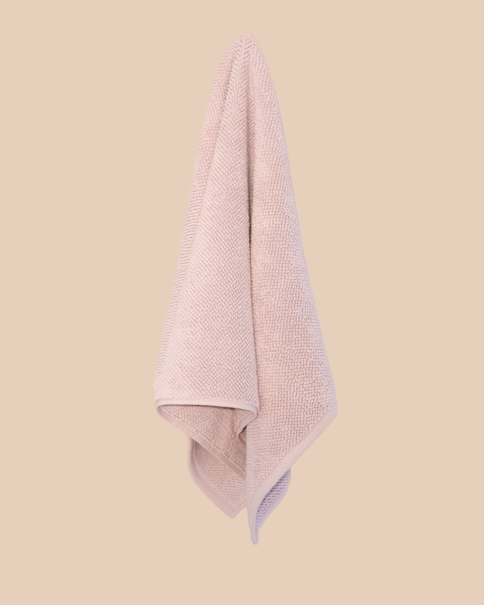 Textured lilac bathmat hanging on a neutral background