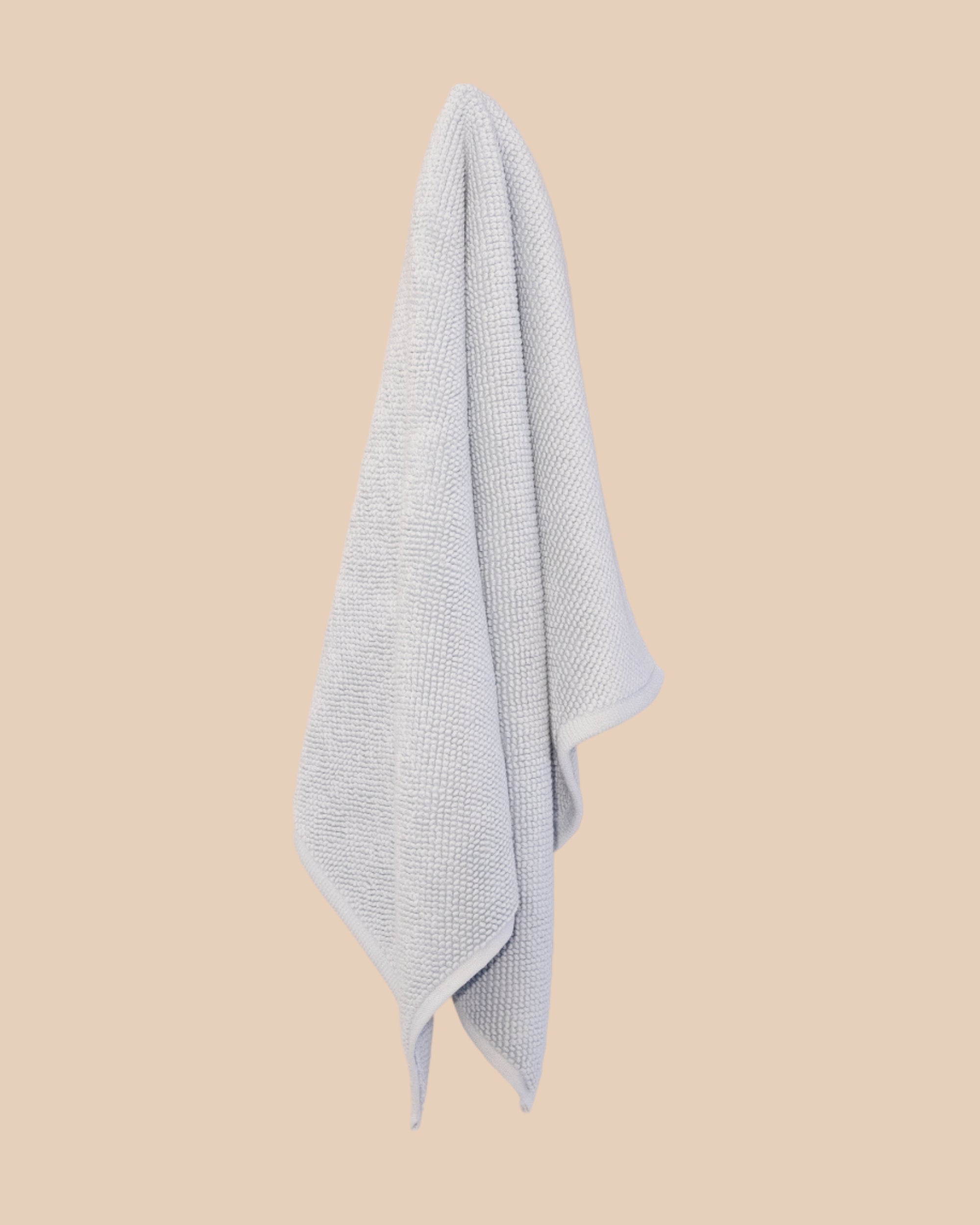 Light blue textured bathmat hanging against a beige background