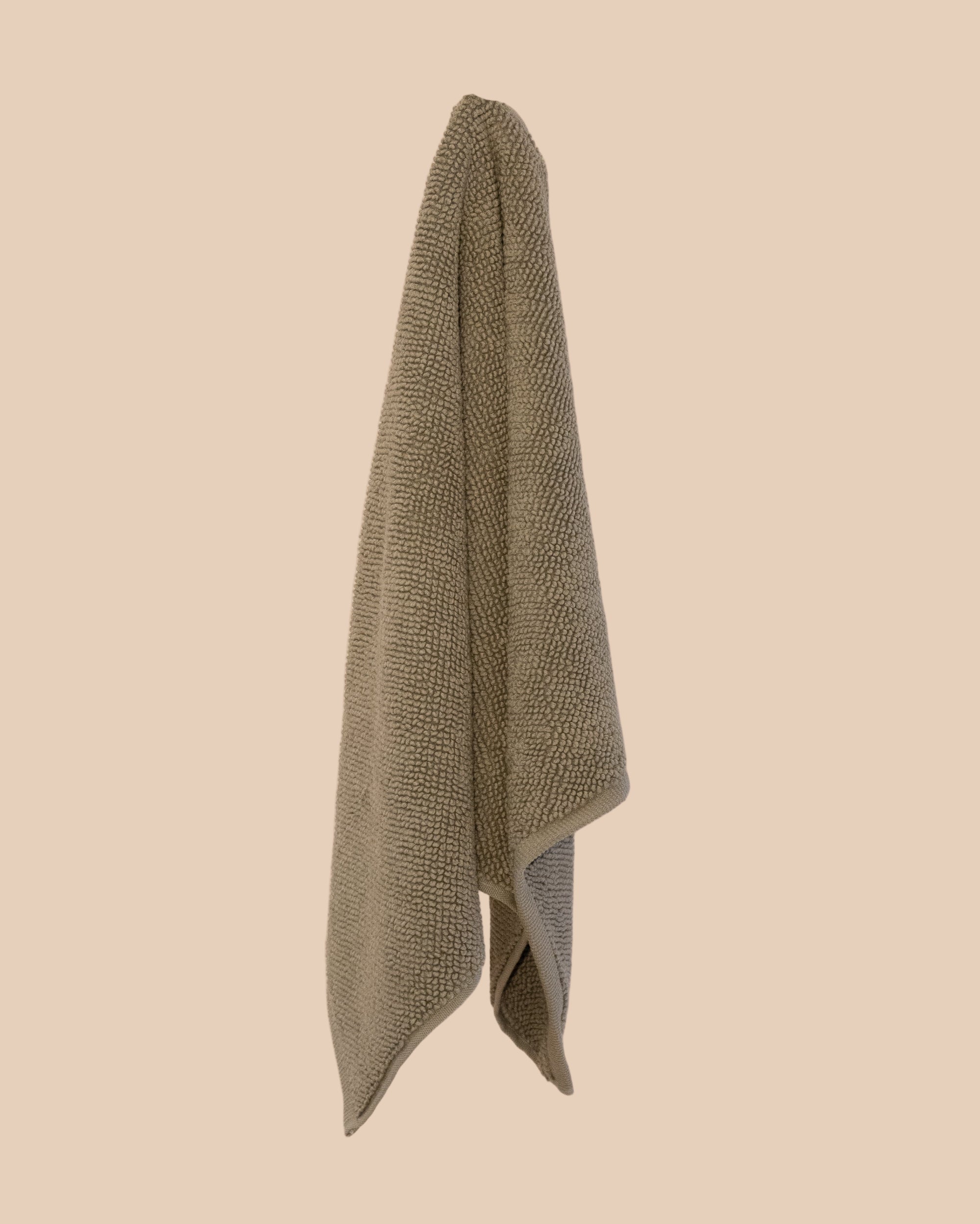 Olive coloured chunky weave cotton bahtmat hanging on a neutral background. 