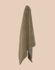 Olive coloured chunky weave cotton bahtmat hanging on a neutral background. 