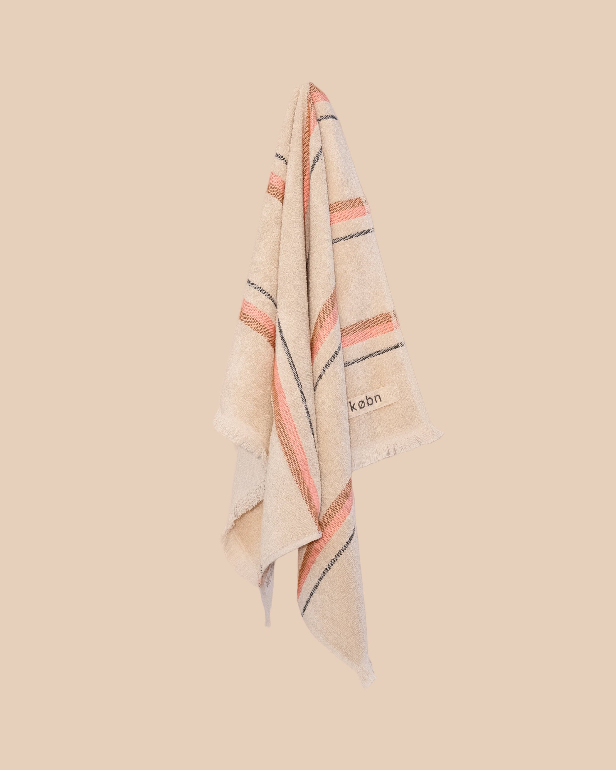 striped hand towel in sand colour with a hot pink and tan stripe hanging on a neutral background. 