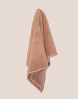 Chunky cotton weave bathmat in soft pink clay colour hanging on a butter yellow background. 