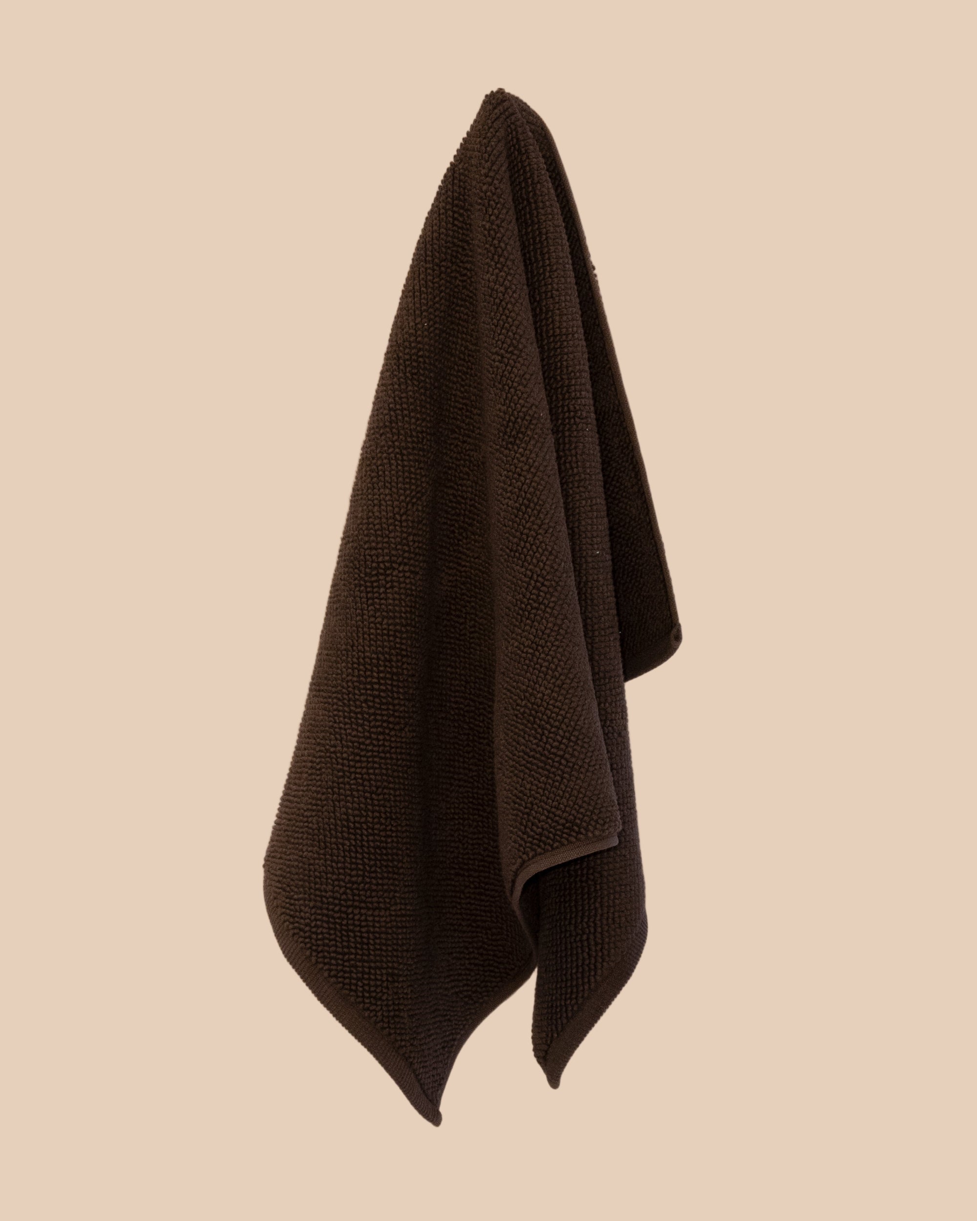 Brown textured bathmat hanging on a beige wall