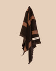 Chocolate brown hand towel with fringing and red and cream stripes hanging on a neutral background. 