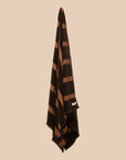 Chocolate brown bath towel with red stripes and fringing hanging on a butter yellow background. 