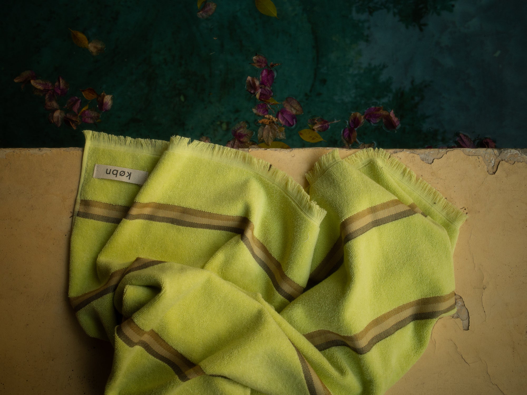 Bright Citrus Kobn towel with stripes and raw edge fringing on edge of pool. 