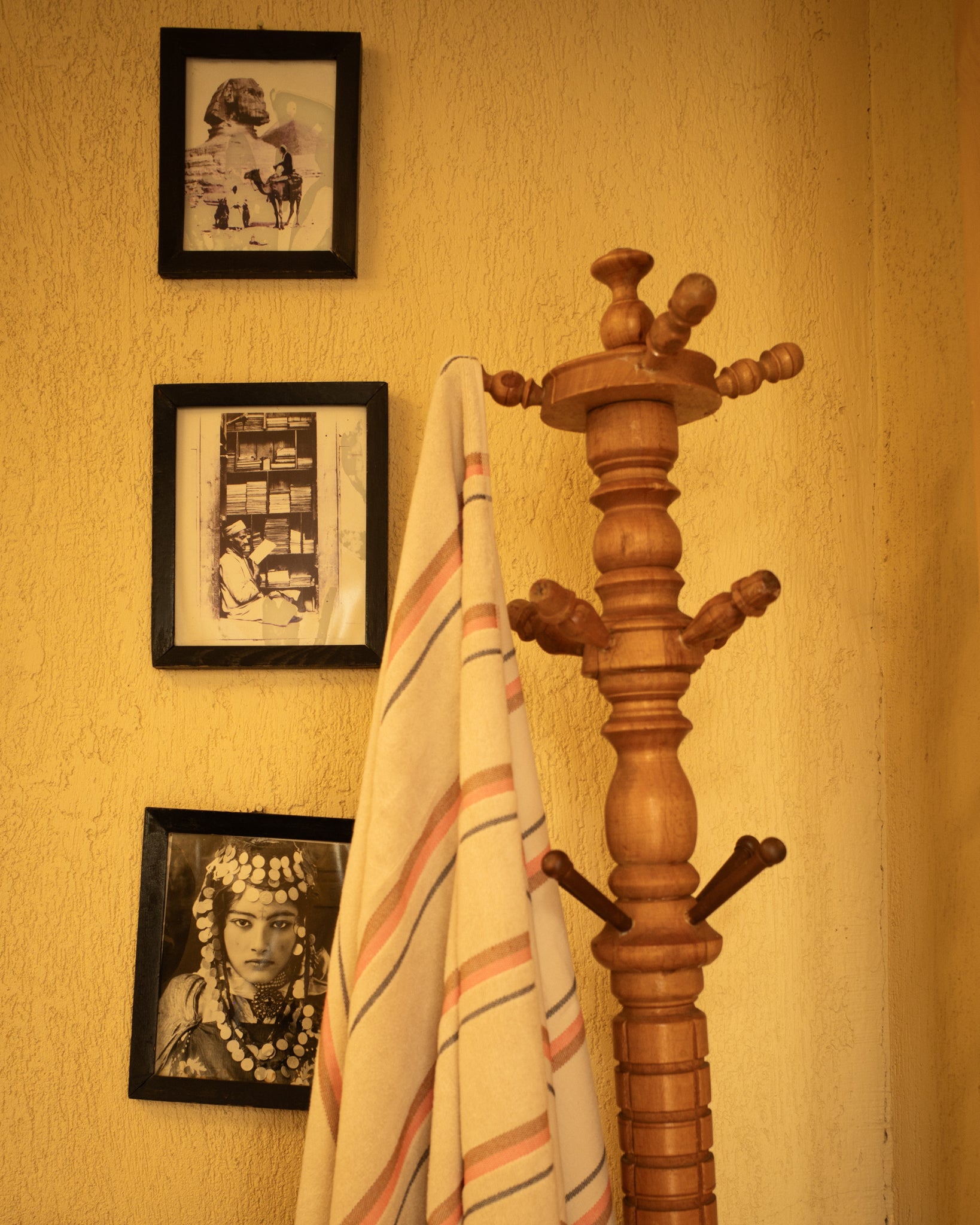 Wooden coat rack with a striped towel against a wall with framed pictures.