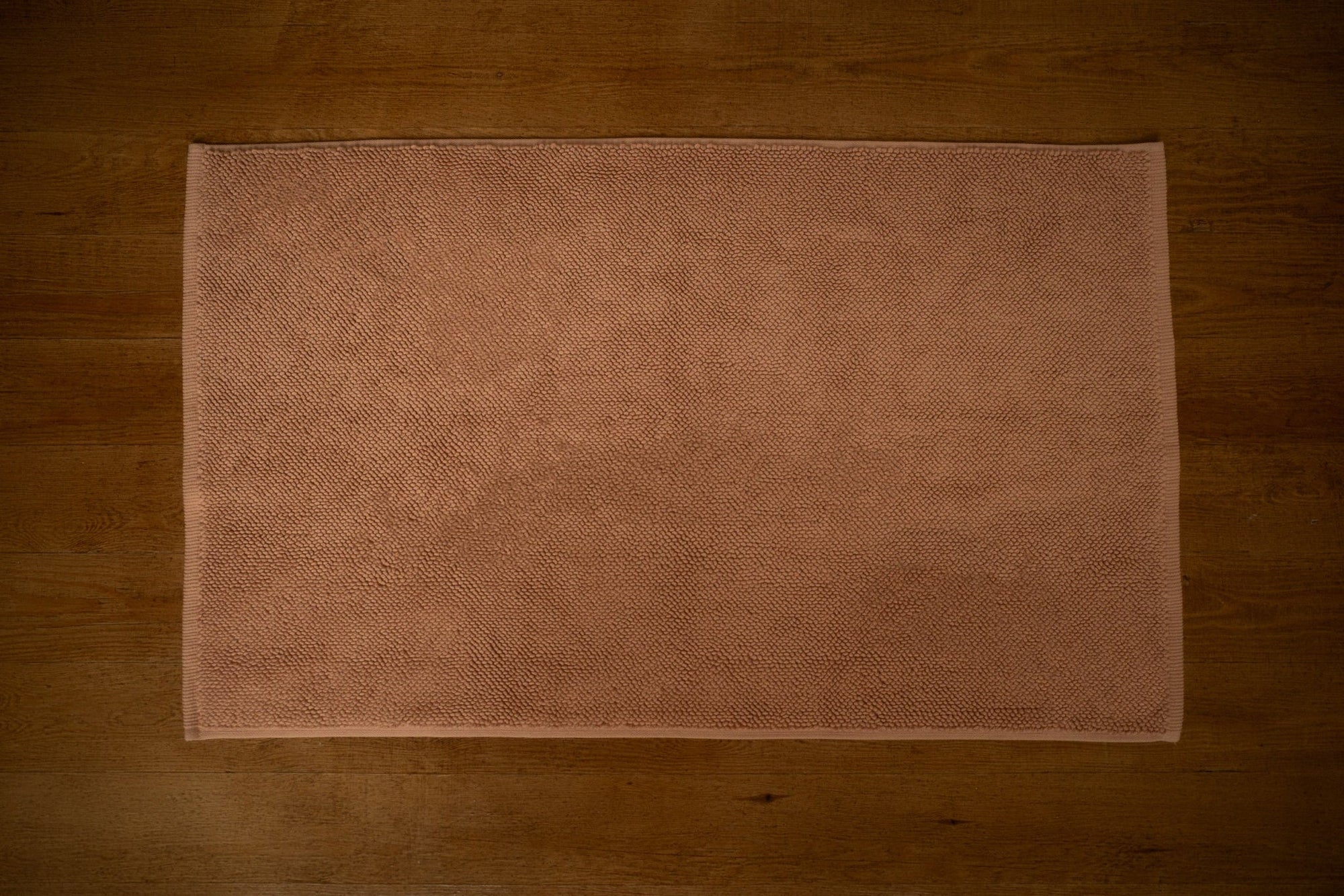 Dussty Pink bath mat on a wooden floor