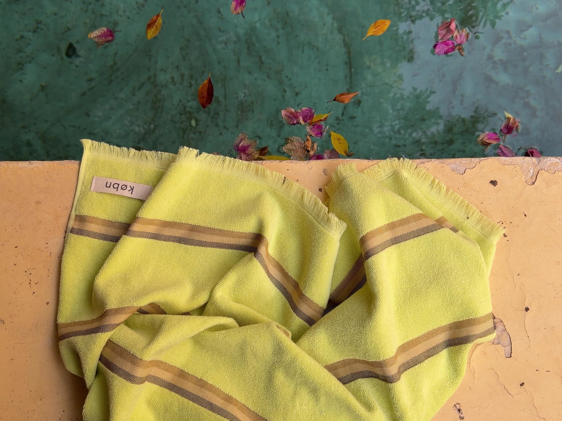 Citrus striped towel poolside with petals and leaves. 