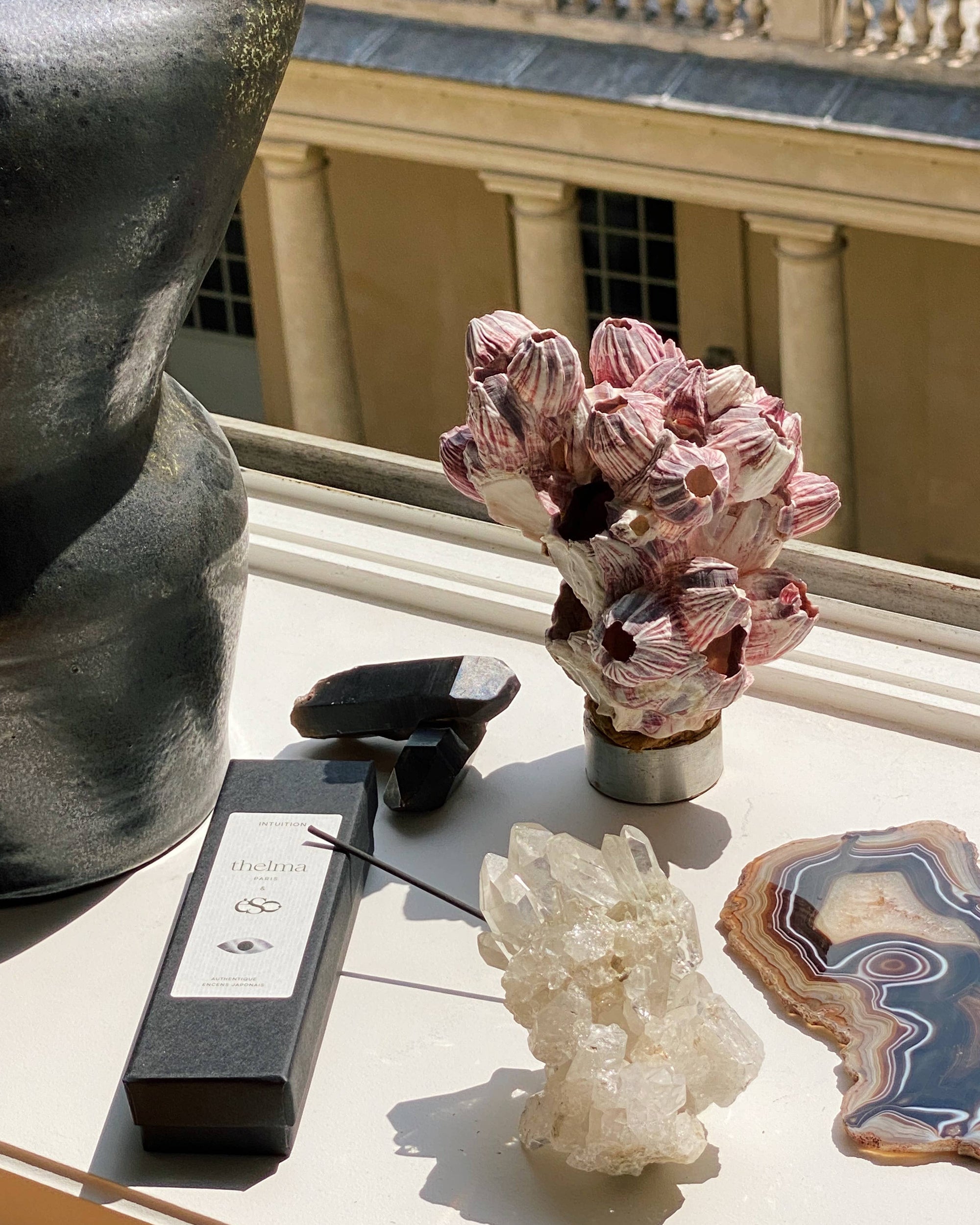 Decorative items including a vase, crystal, and agate on a surface with classical architecture in the background.